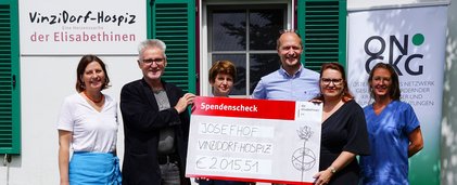 6 Personen nebeneinander. Person in der Mitte hält einen großen Scheck vor sich